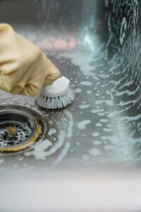 A Person in Yellow Rubber Gloves Cleaning Stainless Sink